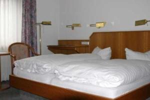 Bett mit einem Kopfteil aus Holz und weißer Bettwäsche in der Unterkunft Hotel Ristorante Ätna in Ulrichstein
