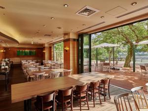 広島市にあるザ ロイヤルパークホテル 広島 リバーサイドの木製のテーブルと椅子、大きな窓のあるレストランを併設しています。