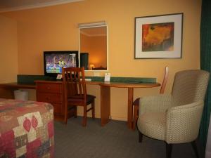Habitación de hotel con escritorio, sillas y TV. en Parramatta City Motel, en Sídney