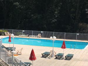 a swimming pool with chairs and red umbrellas at Les chambres et studios Camping Parc de Paletès in Saint-Girons