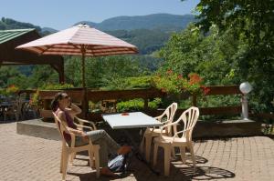 a woman sitting at a table with an umbrella at Les chambres et studios Camping Parc de Paletès in Saint-Girons