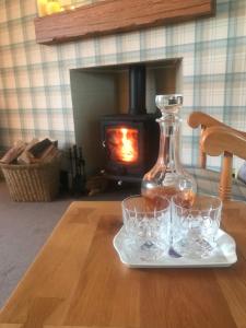 a table with glasses and a bottle on a table with a fireplace at Garden Cottage in Gartocharn