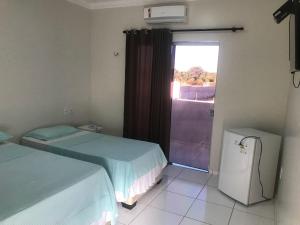 a room with two beds and a window and a refrigerator at Pousada Aerogrill in Juazeiro do Norte