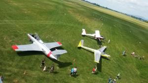 a group of people standing around two planes in a field at AeroCafe in Partizánske