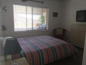 a bedroom with a bed with a striped blanket and a window at Tomaree Lodge in Nelson Bay