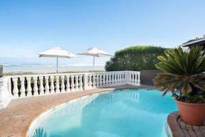 a swimming pool with a fence and an umbrella at The Beach Villa in Melkbosstrand