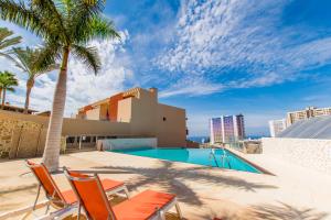 einen Pool mit Stühlen und Palmen sowie ein Gebäude in der Unterkunft Paraiso Pool and Sea View - TENESOL RENTALS in Adeje