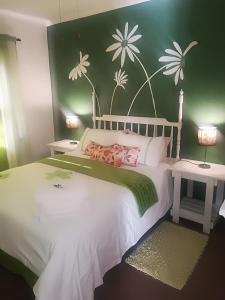 um quarto com uma cama branca com flores pintadas na parede em Tirzah's B&B and Self Catering em Bredasdorp