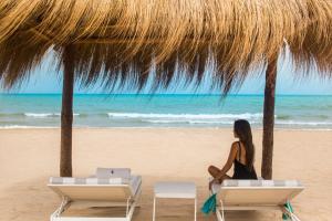 a woman sitting on the beach under a straw umbrella at Four Seasons Hotel Tunis in Gammarth