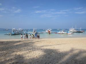 un grupo de personas de pie en una playa con barcos en el agua en Sulu Plaza en Boracay