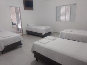 a room with three beds and a window and a mirror at Hotel farol de Minas in Alpinópolis