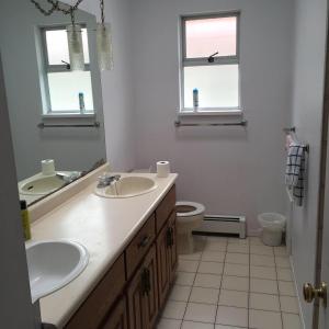 a bathroom with two sinks and a toilet and two windows at Sandy's House in Vancouver