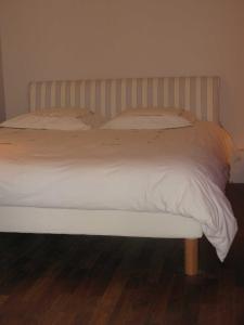 a bed with white sheets and pillows on a wooden floor at Maison des Bois in Bièvres