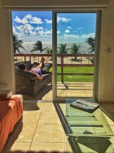 a woman laying on a couch on a balcony with a view of the ocean at Manga Verde Beach Residence in Itamaracá