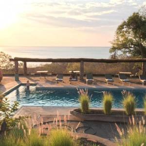 a swimming pool with chairs and the ocean in the background at Musungwa Safari Lodge in Shanjungu
