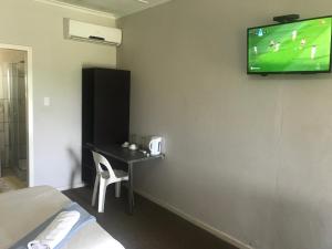 a room with a television on a wall with a desk at Amble Inn Guest House in Empangeni