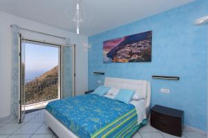 een blauwe slaapkamer met een bed en een groot raam bij DOMUS VIGNA Fusco, Vista Mare, Amalfi Coast in Praiano