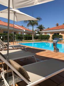 a swimming pool with chairs and an umbrella at Los Leones Bungalows in Maspalomas