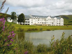 a large white building with a lake in front of it at Macdonald Cardrona Hotel, Golf & Spa in Peebles