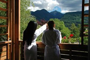 two women standing on a balcony looking out at the mountains at Olimpionico Hotel in Castello di Fiemme