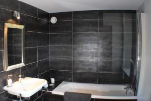 y baño de azulejos negros con lavabo y bañera. en Auberge de la vallee de la gorre, en Saint-Auvent