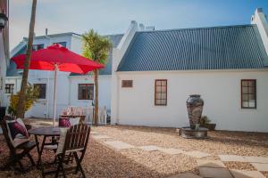 eine Terrasse mit einem Tisch und einem roten Regenschirm in der Unterkunft Aan de Oever Guesthouse in Swellendam