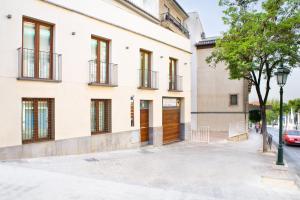 a white building with a wooden door and a tree at Real de Cartuja Apartments & Suites in Granada