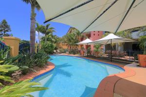 a large swimming pool with umbrellas and palm trees at Kacy's Bargara Beach Motel in Bargara