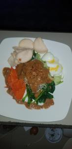 a white plate of food with vegetables and meat at Reynold Artha Guest House in Nusa Lembongan