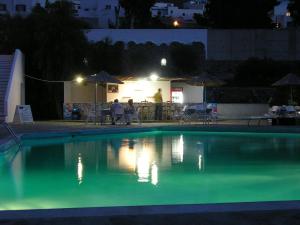 a swimming pool at night with people sitting around a table at Eri Hotel in Parikia