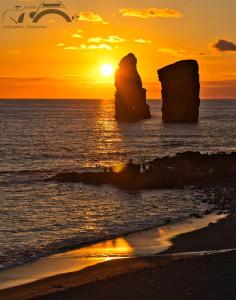 a sunset over the ocean with a rock formation at Casa Dos Mosteiros in Mosteiros