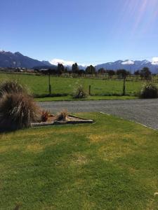 a road with a grass field and mountains in the background at Acheron Cottages in Manapouri
