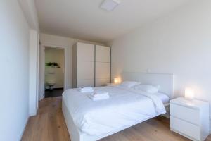 a white bedroom with a large white bed and two lamps at Seaview Zeebrugge in Zeebrugge