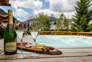 dos copas de vino y queso en una bandeja junto a la piscina en Hotel Cirelle Suite & Spa, en Canazei