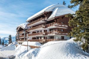 un bâtiment avec un toit recouvert de neige au-dessus d'un sol recouvert de neige dans l'établissement CGH Résidences & Spas Chalet Les Marmottons, à La Rosière