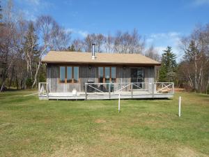 a small house with a large porch in a field at Shaw's Hotel & Cottages in Brackley Beach