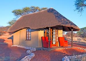 una pequeña casa con techo de paja y sillas rojas en Camelthorn Kalahari Lodge, en Hoachanas