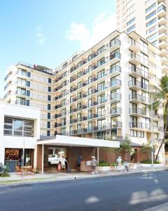 um grande edifício de apartamentos branco com pessoas em pé na frente dele em The Surfjack Hotel & Swim Club em Honolulu