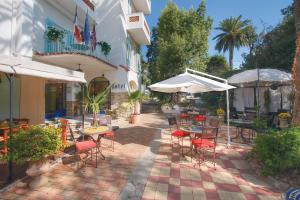 un patio al aire libre con mesas, sillas y sombrillas en Hôtel Le Pré Catelan, en Juan-les-Pins