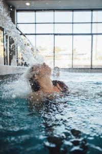 een vrouw in een zwembad besproeid met water bij Domaine du Ferret Restaurant & Spa in Cap-Ferret