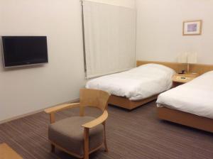 a hotel room with two beds and a chair and a tv at Furano Hotel in Furano