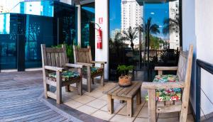3 Stühle und ein Tisch auf einer Veranda mit einem Fenster in der Unterkunft Bahamas Suíte Hotel in Campo Grande