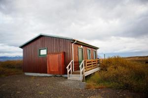 a small red cabin with a wooden door and a porch at Hestaland Riverside Cottage in Staðarhús +16 photos