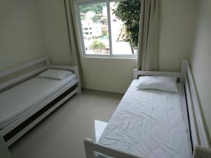Habitación pequeña con 2 camas y ventana en Apto no centro de Bombinhas, en Bombinhas