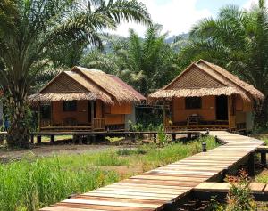 two small huts with a wooden bridge and palm trees at Khao Sok Blue Mountain in Khao Sok