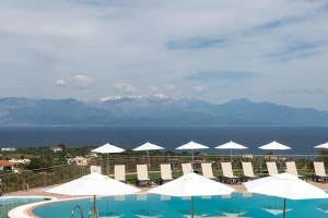 una piscina con sombrillas y sillas blancas y el océano en Baywatch Hotel, en Chrani