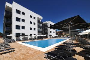 a swimming pool with chairs and umbrellas next to a building at Leo Deluxe Punta Umbría in Punta Umbría