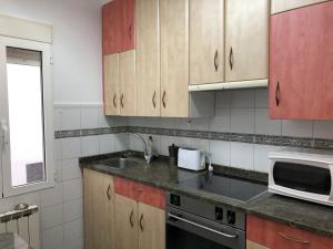 eine Küche mit Holzschränken, einer Spüle und einer Mikrowelle in der Unterkunft Puerta Del Carmen in Saragossa