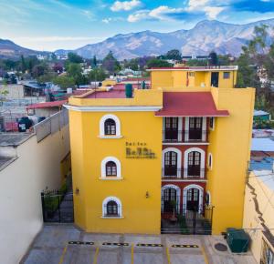 um edifício amarelo com um telhado vermelho com montanhas ao fundo em Suites Bello Xochimilco by DOT Tradition em Oaxaca de Juárez