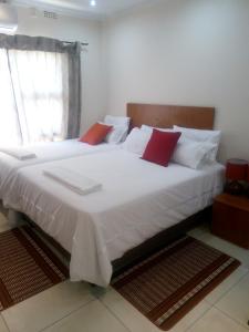 una camera da letto con un grande letto bianco con cuscini rossi di Eros Guest Inn a Francistown